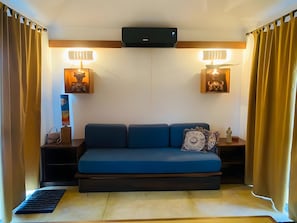 Tunnelmallinen huone, jossa on sininen sohva, kaksi seinälle asennettua lamppua, litteänäyttöinen televisio ja pieni pöytä, jonka päällä on koriste-esineitä.