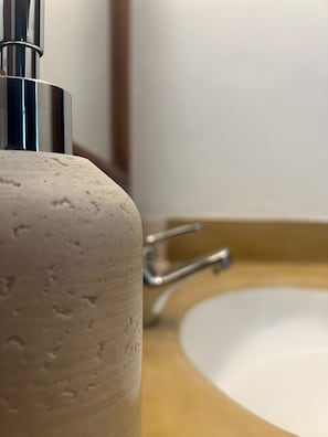 Kylpyhuoneen allas, jossa on krominen hana ja beigenvärinen, kuvioitu taso.