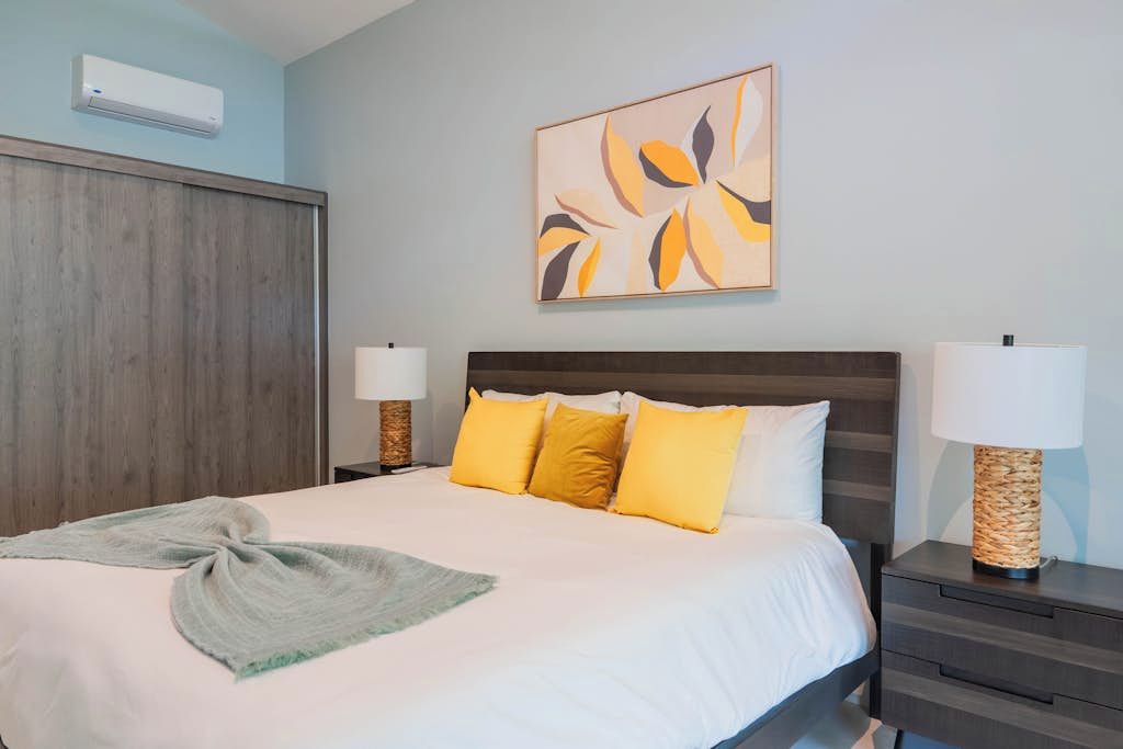 Una camera d'albergo con un letto, lampade ai comodini, un condizionatore d'aria a parete e un quadro.