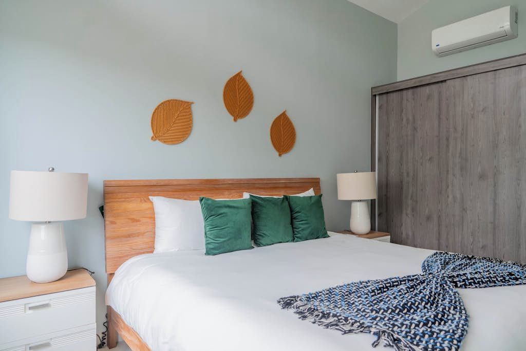 Quarto de hotel com cama, duas luminárias de cabeceira, cabeceira de madeira, ar-condicionado fixado na parede e uma janela grande.