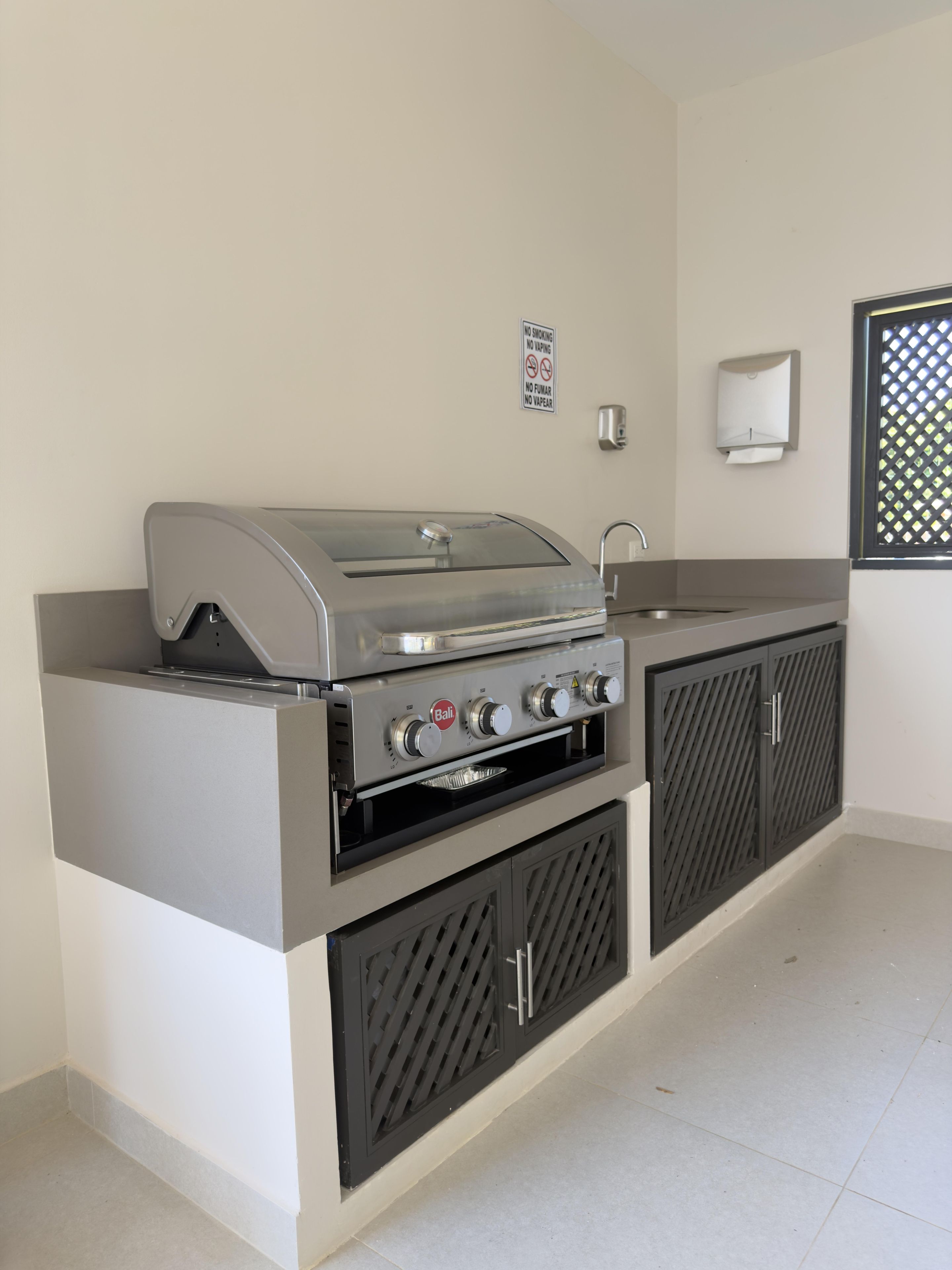 A kitchen with a built-in grill, a sink, and a wall-mounted soap dispenser.