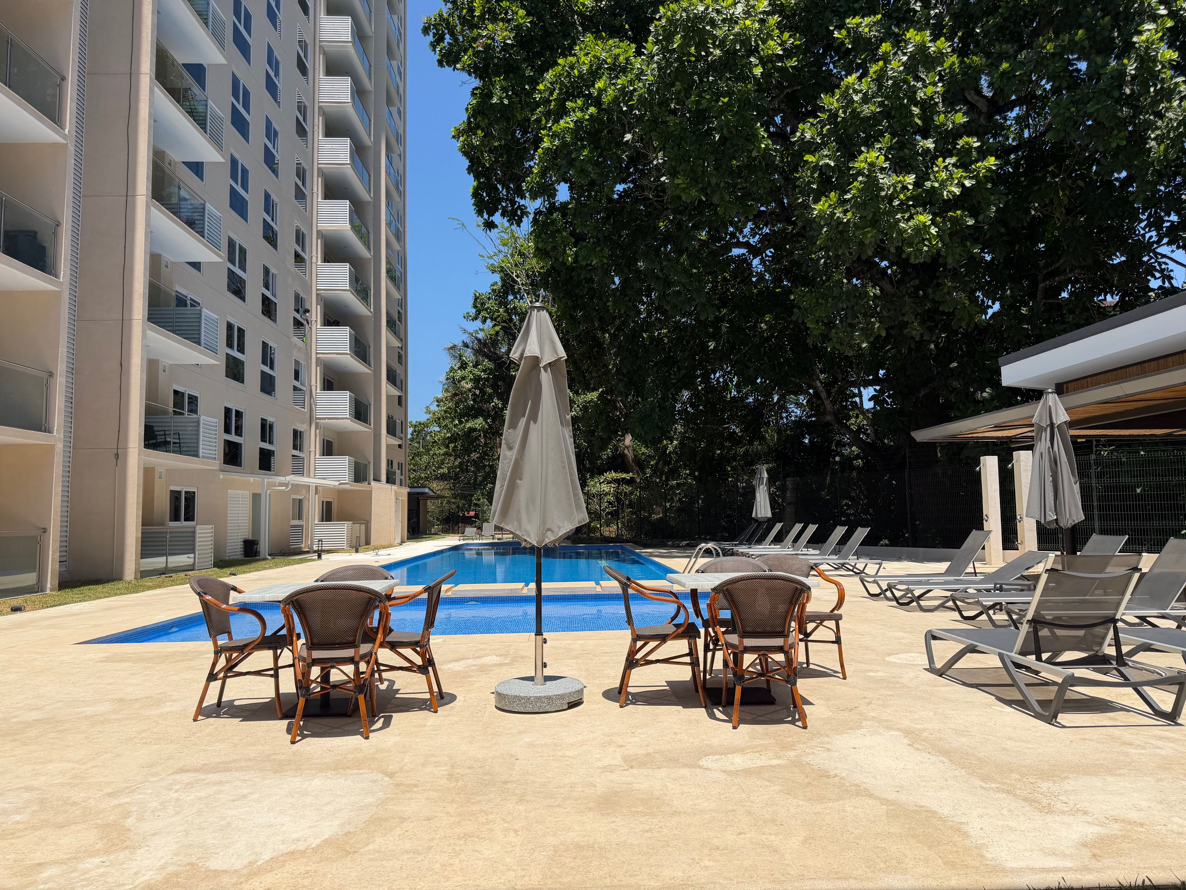 Ein Swimmingpool mit Liegestühlen und Sonnenschirmen, umgeben von einem Gebäude mit Balkonen.