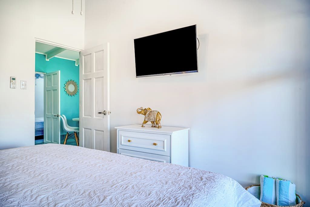 A bedroom with a bed, a white dresser, a television mounted on the wall, and a door leading to another room.