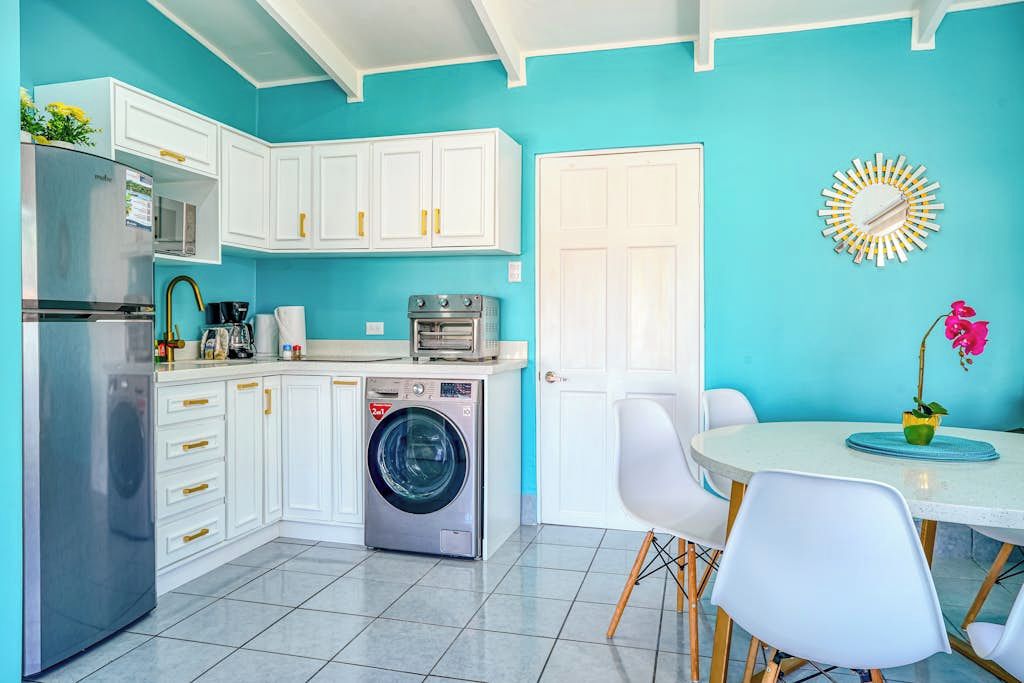 A compact kitchen with white cabinets, a washing machine, a refrigerator, and a dining area with a table and chairs.