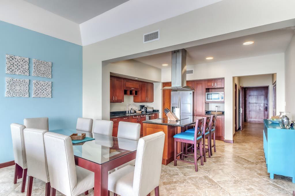 A modern kitchen with a central island, wooden cabinets, and a dining area with a glass table and chairs.