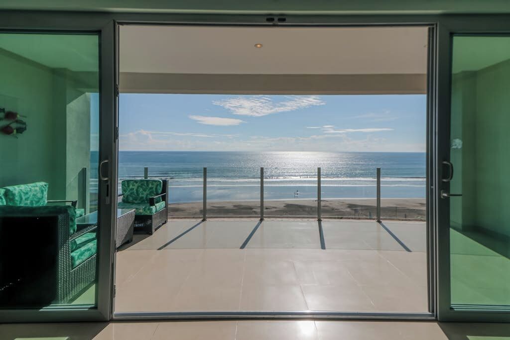 Ein Zimmer mit Glastür, das auf einen Balkon mit Blick auf einen Strand führt.
