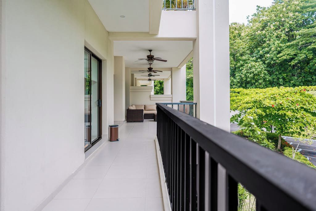 A balcony with a ceiling fan, a trash bin, and a seating area with a sofa and a table.