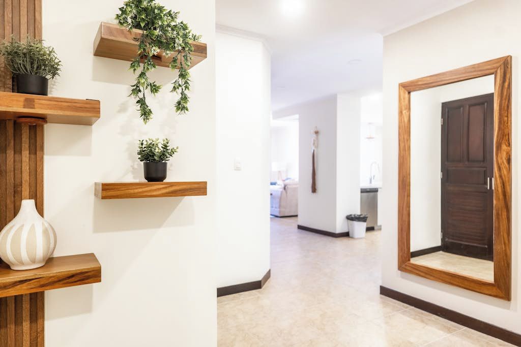 Een gang met houten planken waarop potplanten en een witte vaas staan, die uitkomt in een kamer met een donkerhouten deur.