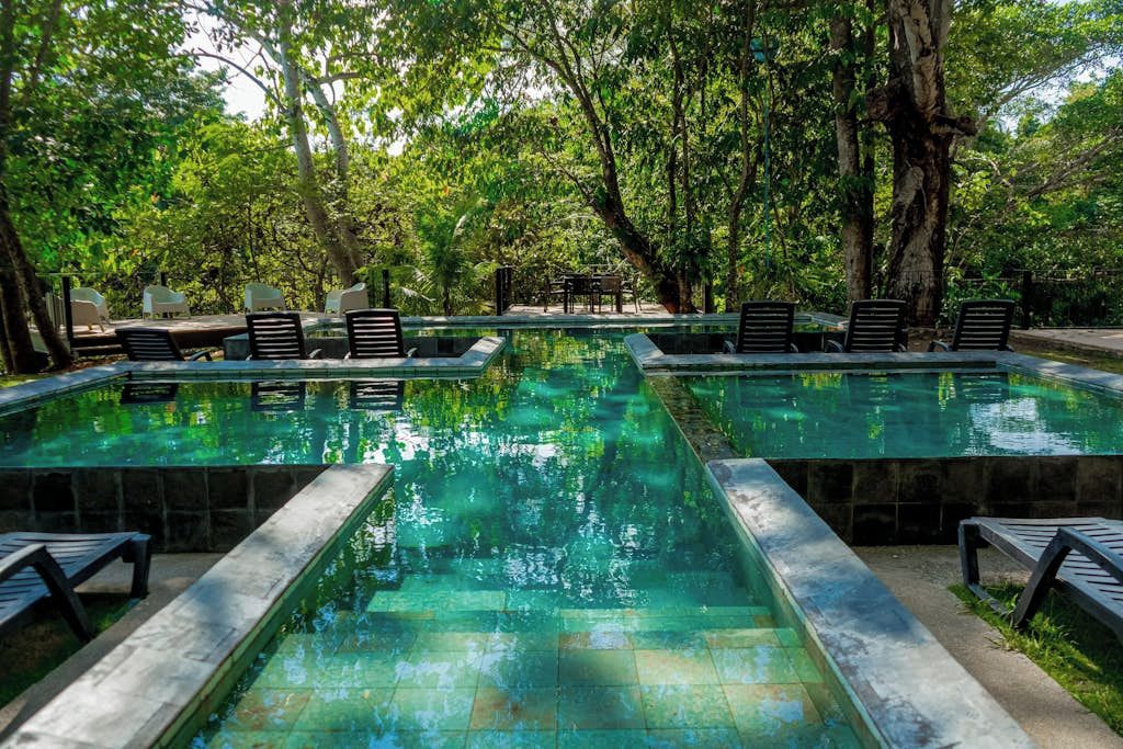 A pool area with lounge chairs and a table, surrounded by trees.