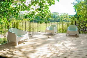 Een houten terras met drie witte plastic stoelen en een metalen hek.
