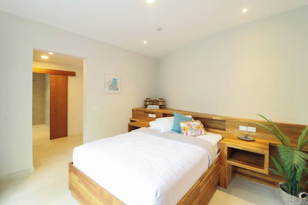 A bedroom with a wooden bed, bedside tables, a nightstand, a wall-mounted shelf, and a potted plant.
