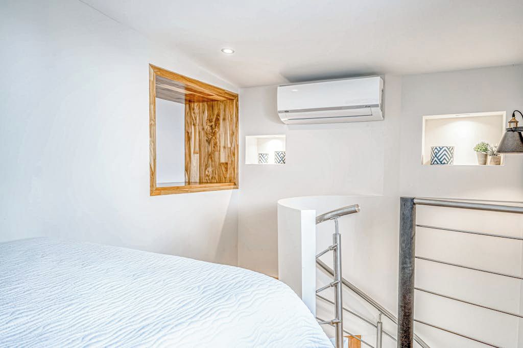 Een slaapkamer met een bed, een raam, een airconditioning, een leuning en een plank met decoratieve objecten.