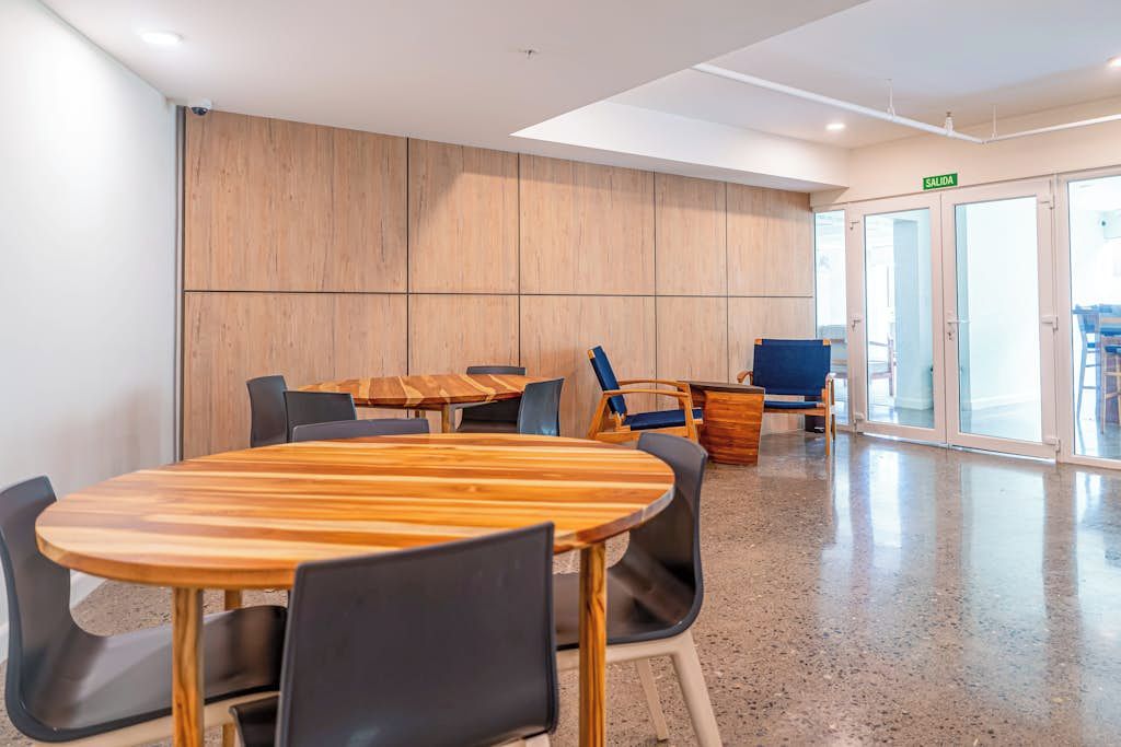 A conference room with a wooden table and chairs, a blue sofa, and a glass door labeled 'SALIDA'.