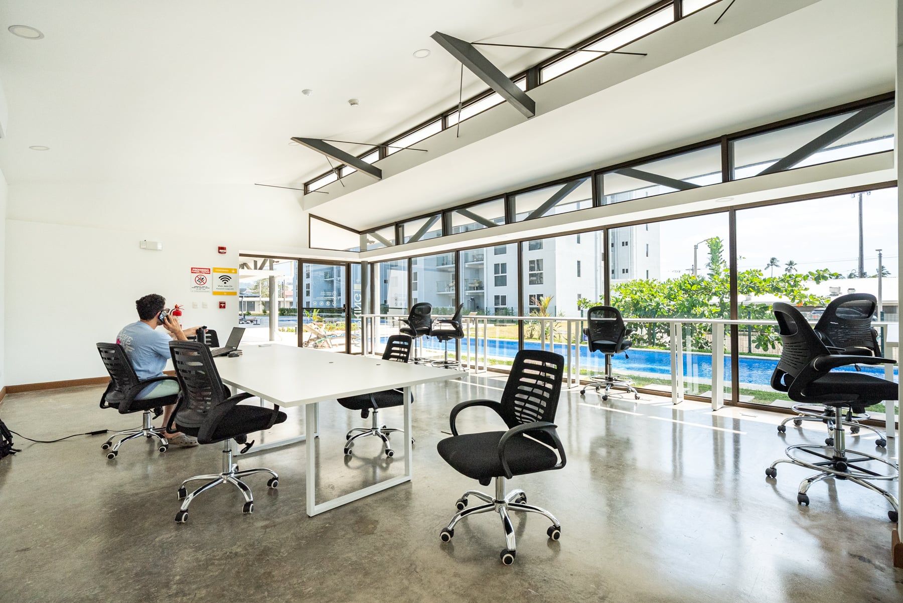 Ein moderner Konferenzraum mit Glastisch, schwarzen Bürostühlen und großen Fenstern mit Blick auf einen Swimmingpool und Gebäude.