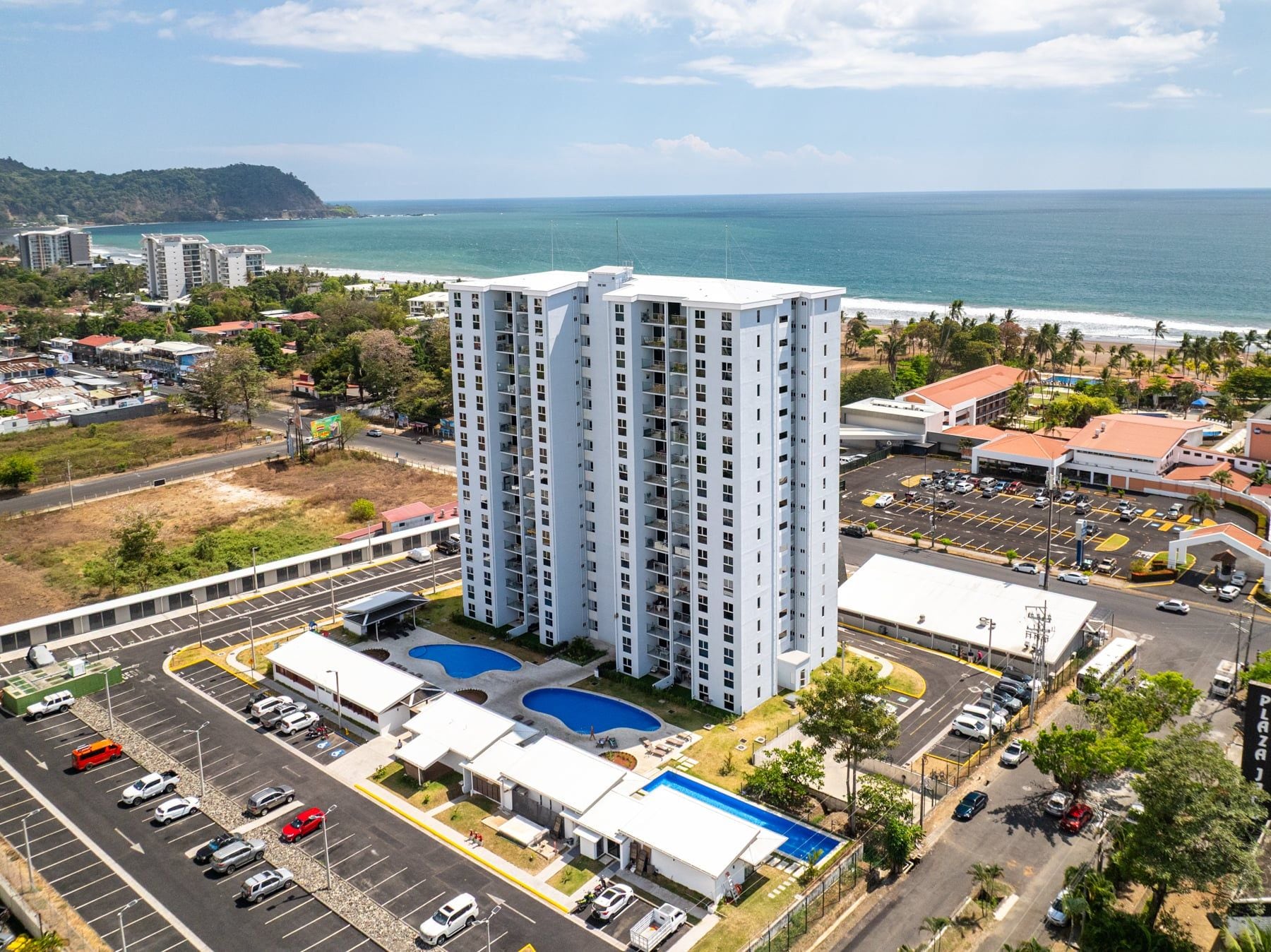 A high-rise hotel with a pool, parking lot, and ocean view.