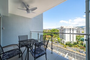 Un balcó amb ventilador de sostre, taula i cadires, i vista sobre un pàrquing i edificis.