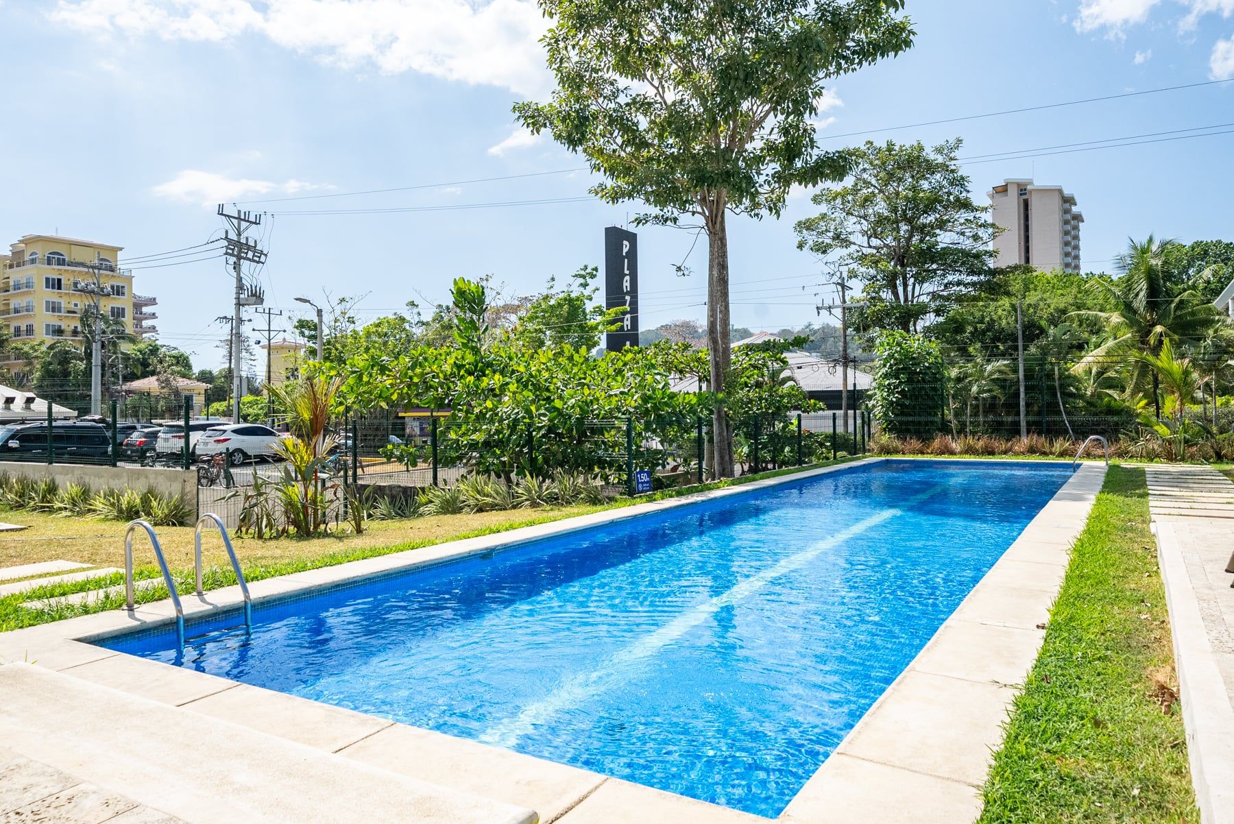 A rectangular swimming pool with a clear blue water surface, surrounded by a concrete deck and a grassy area.