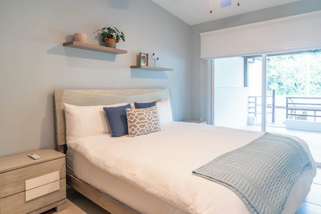 A bedroom with a large bed, a bedside table, and a view of the outdoors.