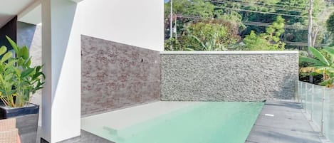 A modern outdoor space with a glass floor leading to a pool, surrounded by a white wall and a stone wall.