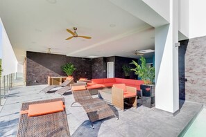 Ein Sitzbereich im Freien mit Korbmöbeln und orangefarbenen Kissen, einem roten Sofa und Deckenventilatoren.