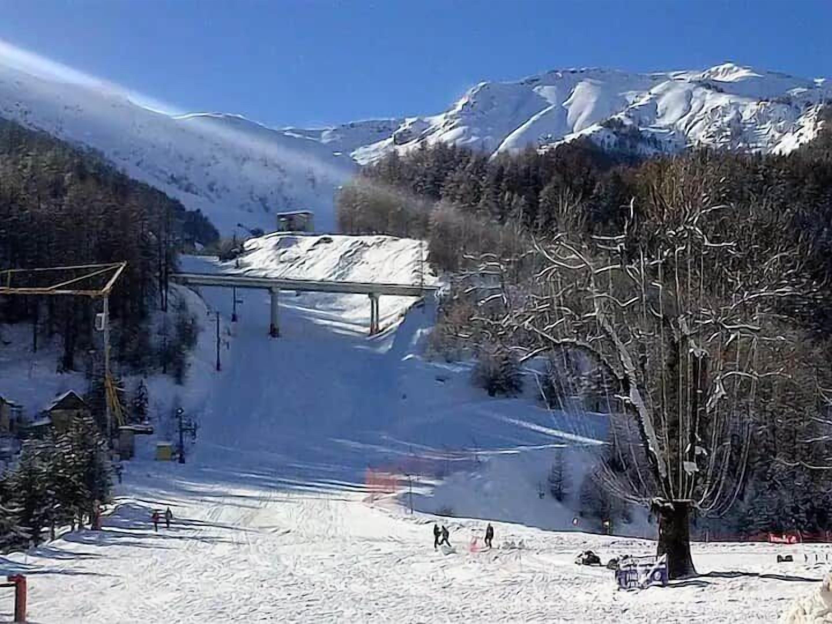 A snow-covered ski slope with a lift station and a tree in the foreground.