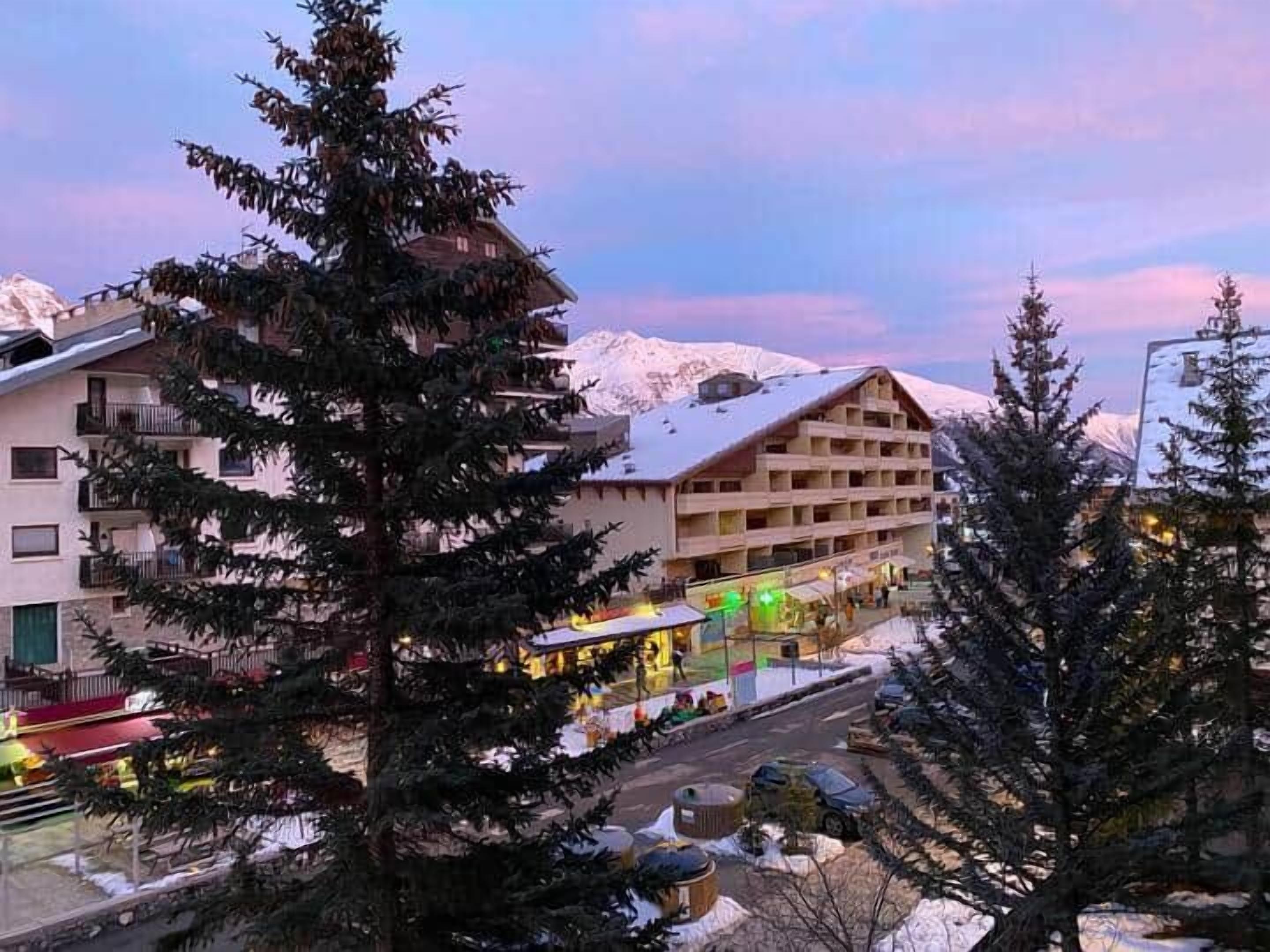 Ett hotell med flera våningar, ett snötäckt berg i bakgrunden och en gata med parkerade bilar.
