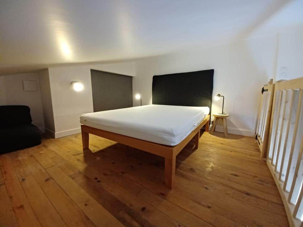 A bedroom with a large bed, a bedside table with a lamp, and a radiator on the wall.