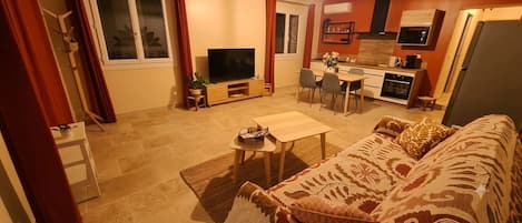 A living room with a sofa, a TV, a dining table, and a kitchen area with a microwave and oven.