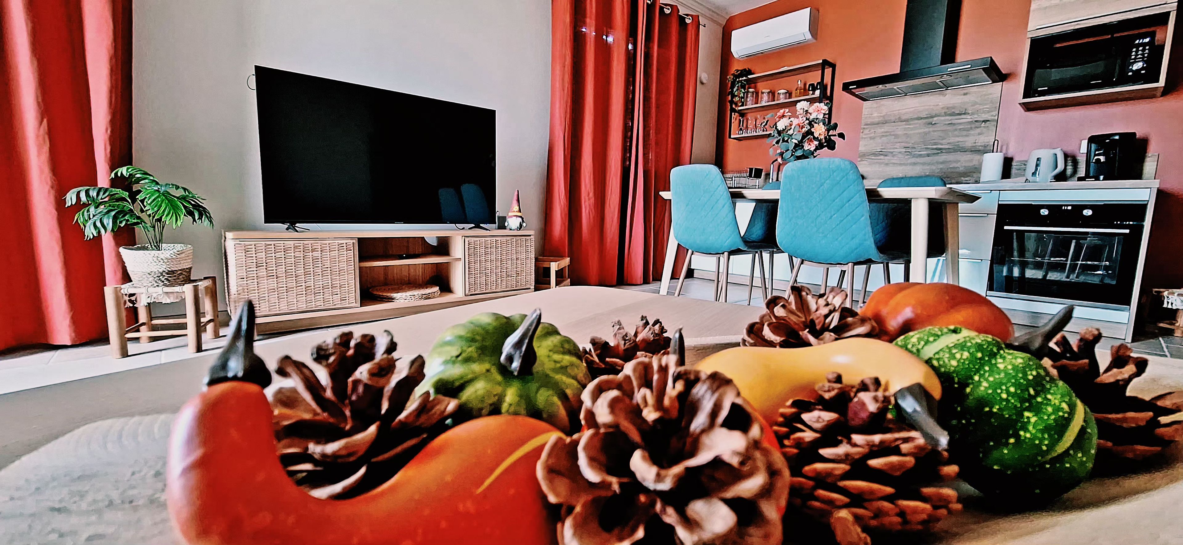 A modern living room with a flat-screen TV, red curtains, a dining area with blue chairs, and a kitchen with a microwave.