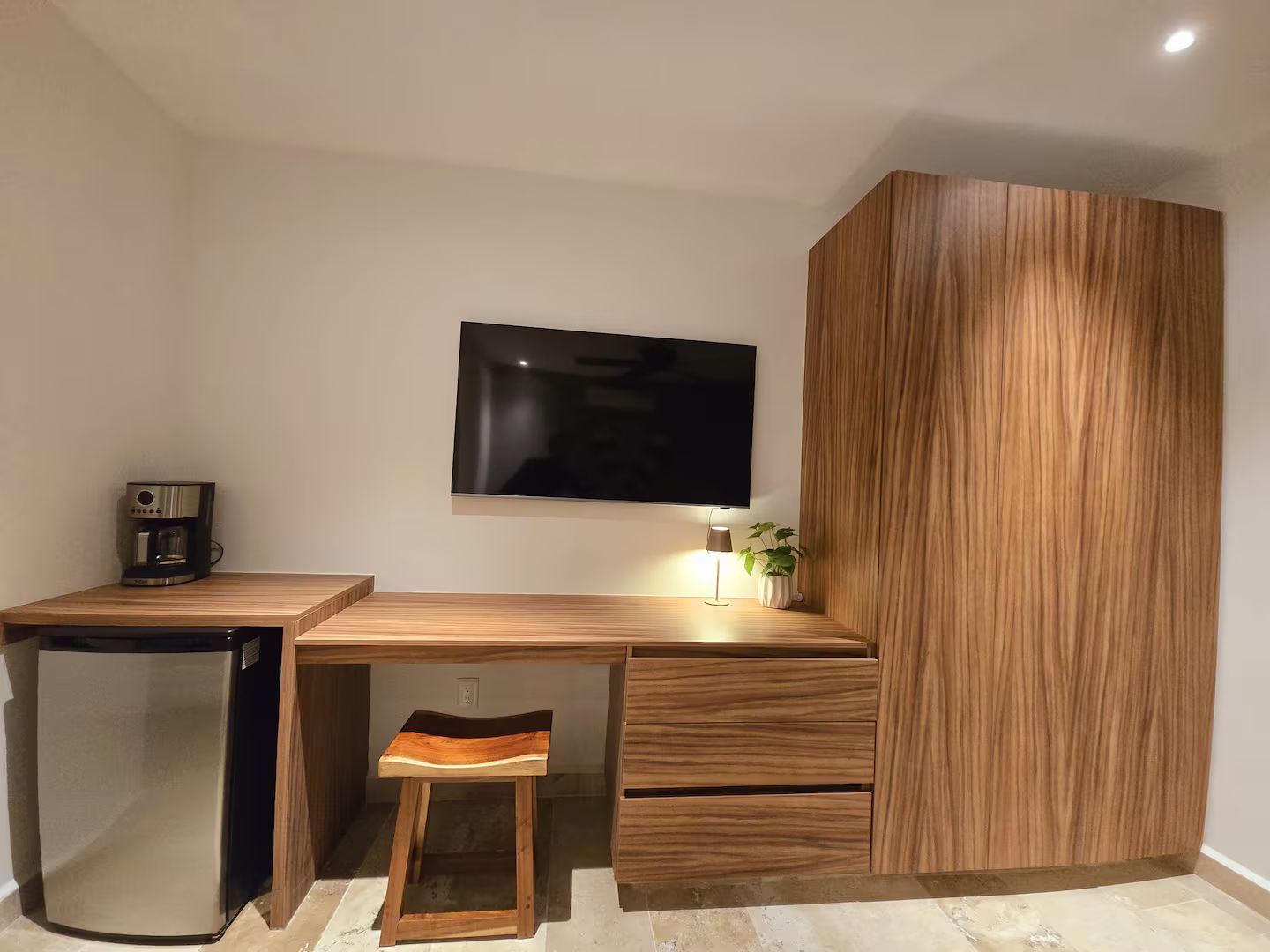 A modern kitchenette with a built-in refrigerator, a coffee maker, and a flat-screen TV mounted on the wall.