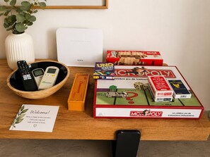 A wooden table with a welcome card, a bowl with remote controls, a white device, and Monopoly game boxes. - Panoramic Sea View Luxury Stay (Agadir)