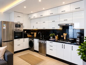 A modern kitchen with stainless steel appliances, white cabinetry, and a black countertop. - Panoramic Sea View Luxury Stay (Agadir)