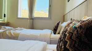 Et hotelværelse med to senge, et vindue med gardiner og udsigt til det fri.