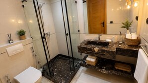 Et stilfuldt badeværelse med et glasafskærmet brusebad, et hvidt toilet, en marmorvask og en trækommode.