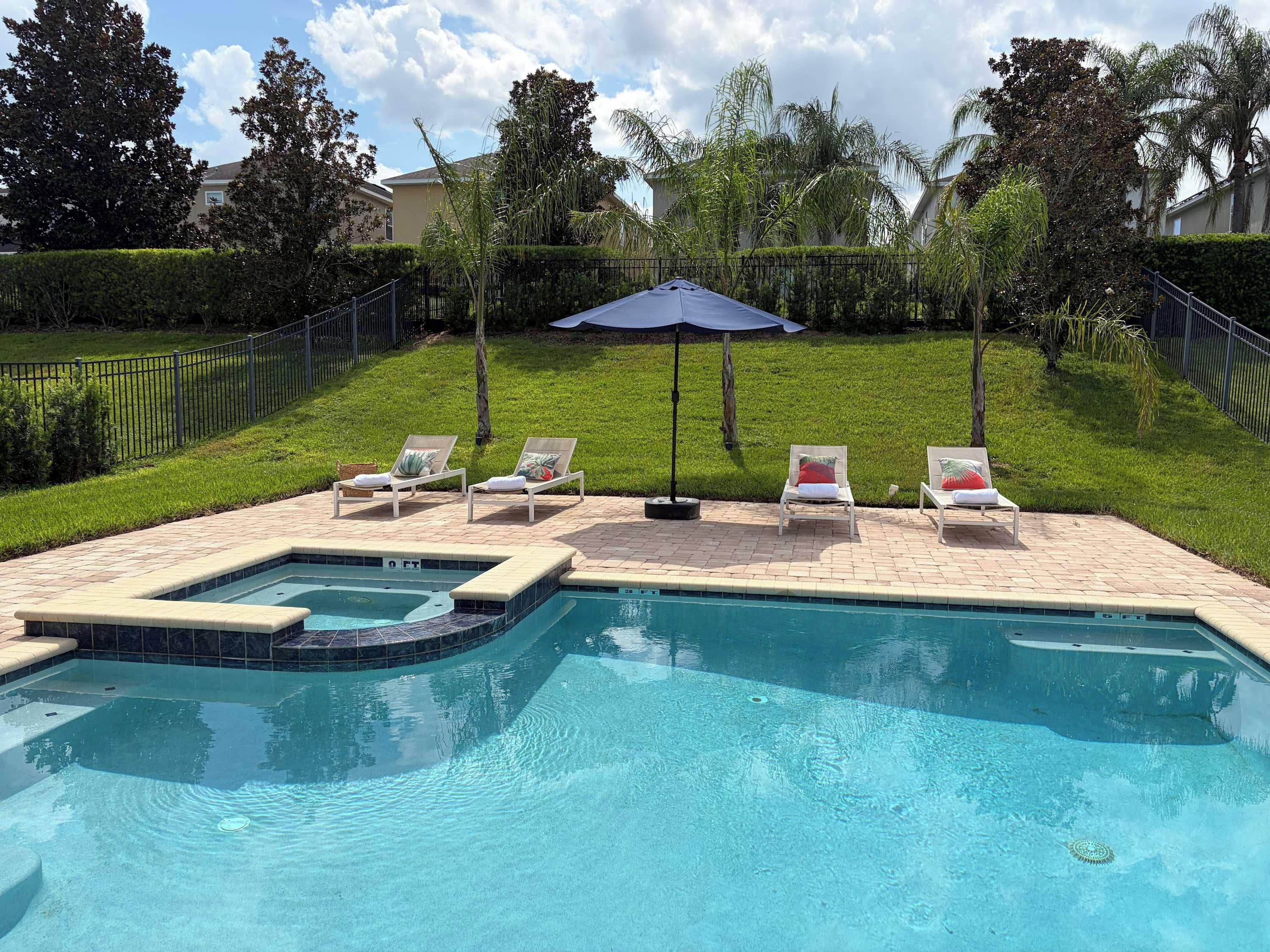 A swimming pool with a hot tub, surrounded by lounge chairs and a covered umbrella.