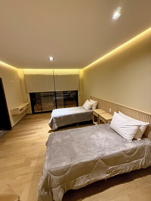 Un dormitorio moderno con dos camas, un banco empotrado y un ventanal grande.