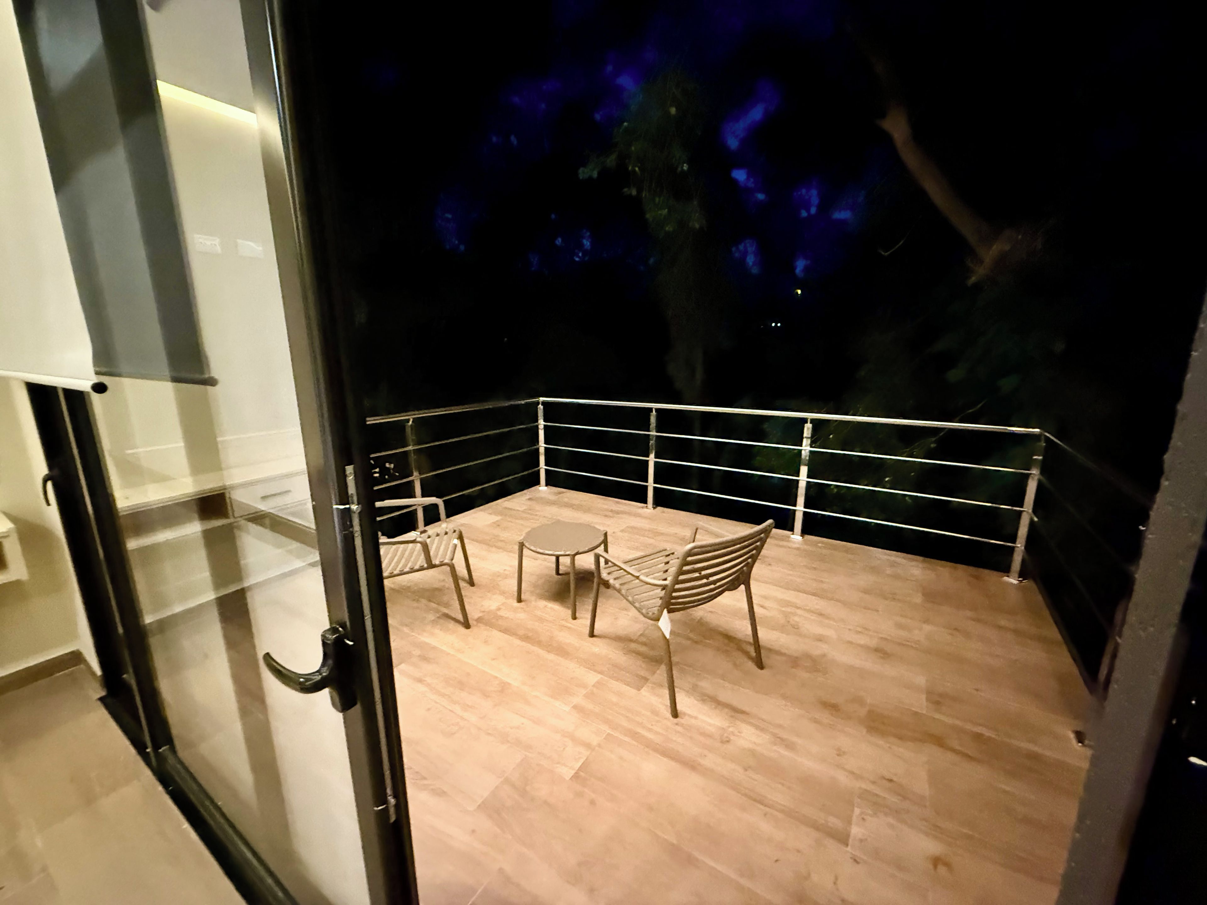 A balcony with a table and chairs, a glass door, and a view of the night sky.