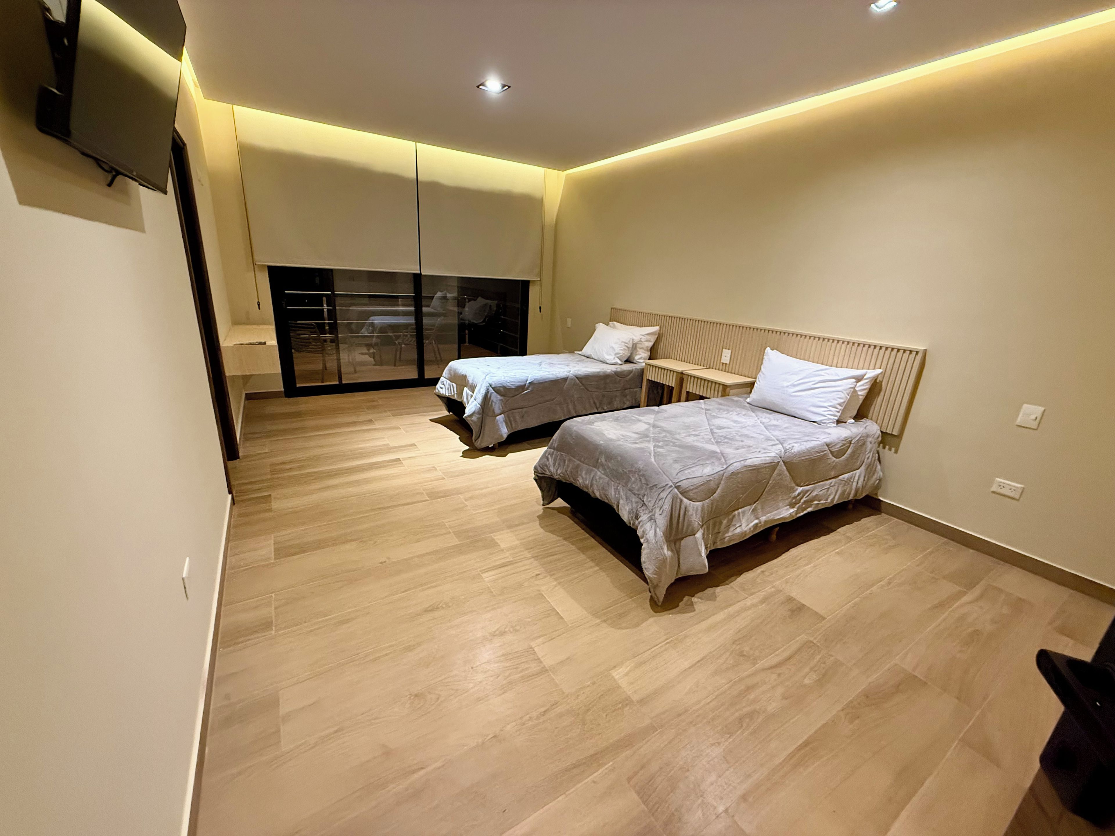 Une chambre moderne avec deux lits, une porte-fenêtre coulissante et un téléviseur à écran plat fixé au mur.