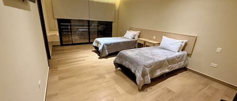 Un dormitorio moderno con dos camas, una puerta corrediza de vidrio y un televisor de pantalla plana montado en la pared.