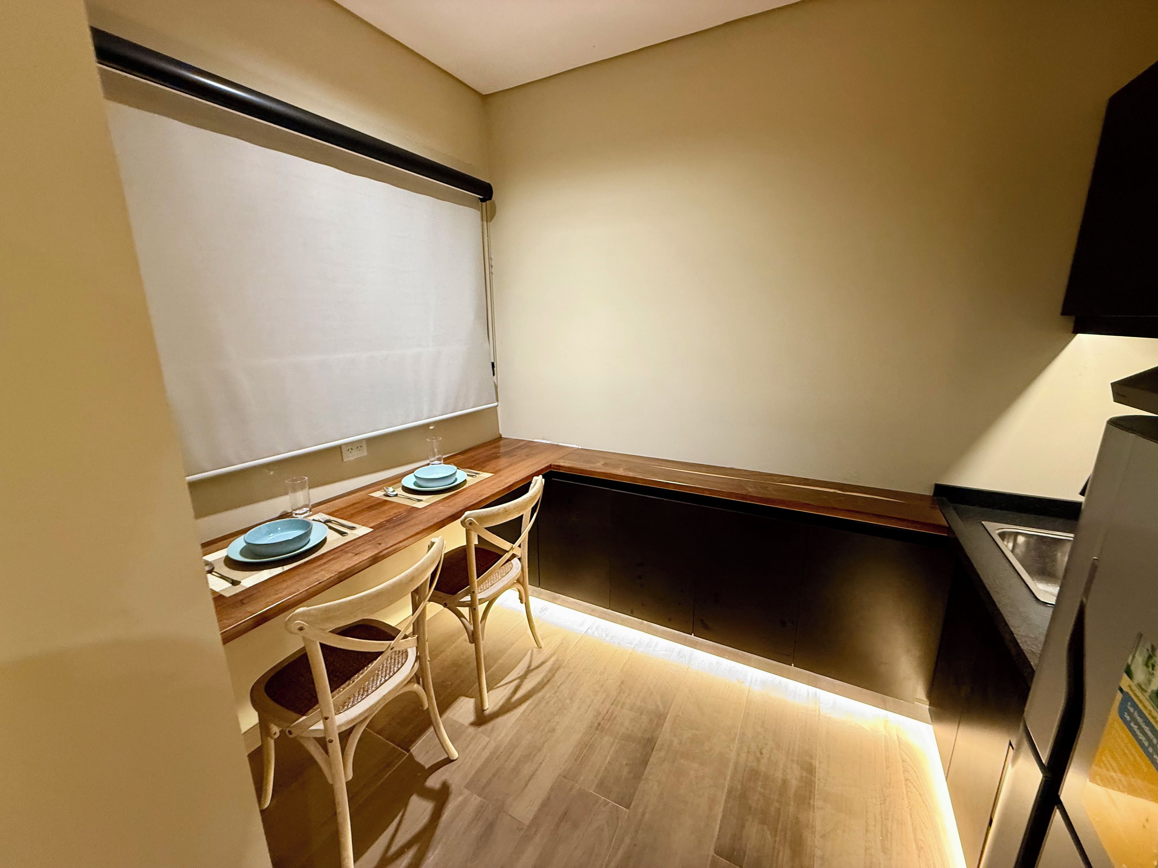 A compact kitchen with a wooden countertop, two chairs, a sink, and a window with a blind.