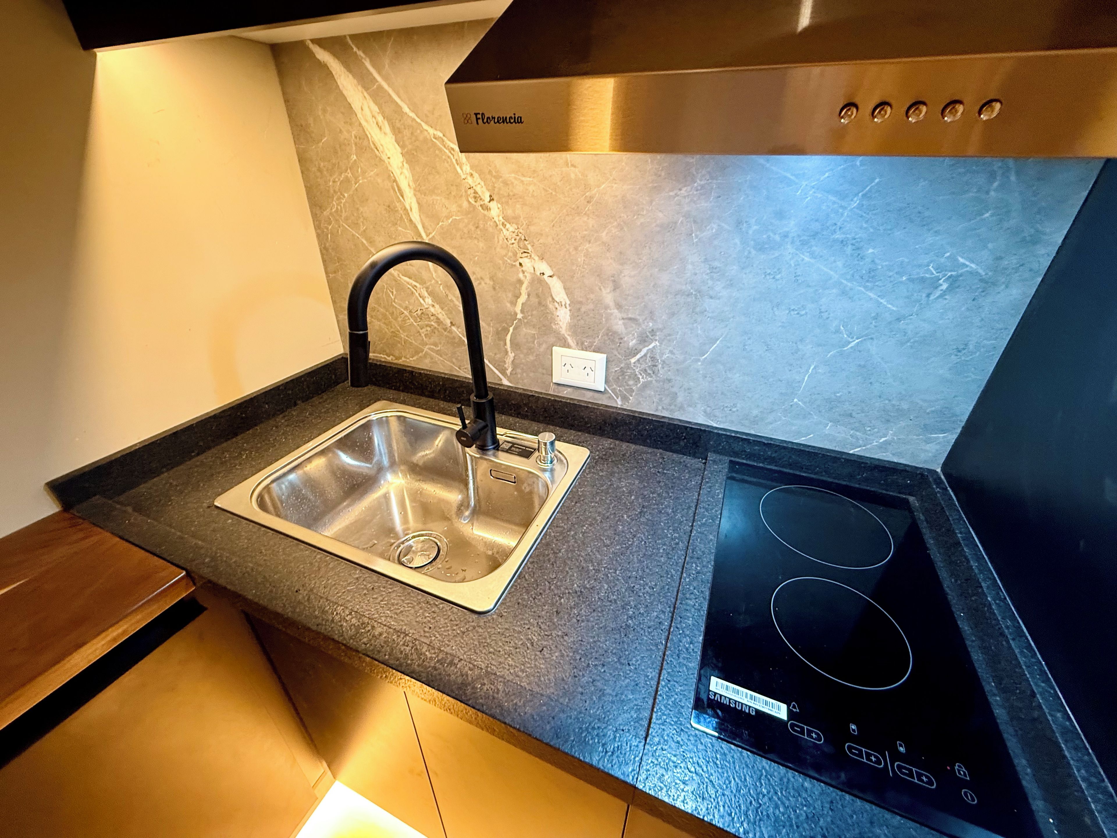 A kitchen with a stainless steel sink, black faucet, and a black induction cooktop.