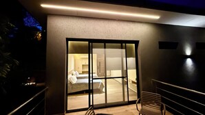 A modern interior with a large sliding glass door leading to a bedroom, a wooden bench, and a staircase. - Minimalist apartment in the jungle (Puerto Iguazú)