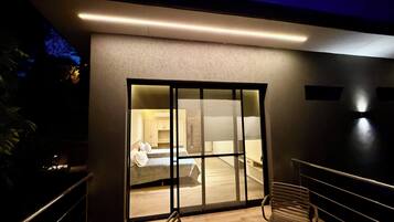 A modern interior with a large sliding glass door leading to a bedroom, a wooden bench, and a staircase.