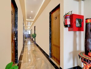 A hotel hallway with a polished marble floor, wooden doors, and a fire extinguisher mounted on the wall. - Deluxe Hotel Rk Heights And Banquets (Varanasi)