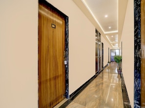 A hallway with a wooden door labeled '208', a marble floor, and a plant in the distance. - Deluxe Hotel Rk Heights And Banquets (Varanasi)