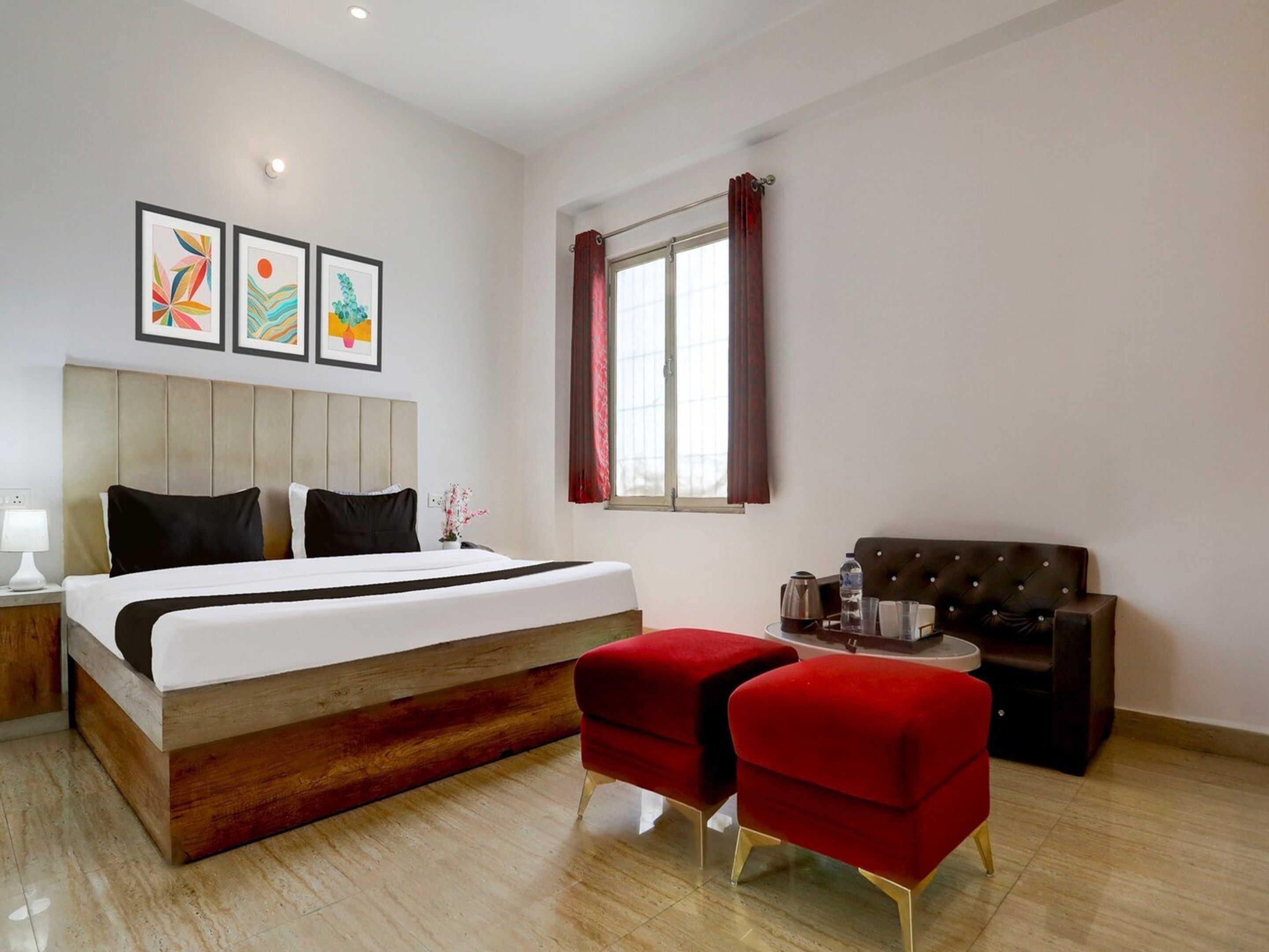 Una camera d'albergo con un letto, un divano rosso, una poltrona rossa, una finestra con tende e tre quadri appesi al muro.