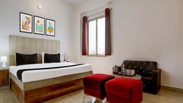 Una camera d'albergo con un letto, un divano rosso, una poltrona rossa, una finestra con tende e tre quadri appesi al muro.
