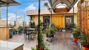 A covered outdoor seating area with tables and chairs, surrounded by potted plants. - Deluxe Hotel Rk Heights And Banquets (Varanasi)