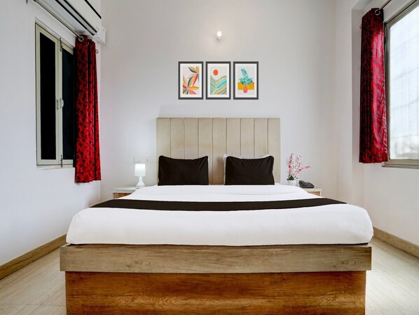 A hotel room with a large bed, a bedside table with a lamp, a phone, and three framed artworks on the wall. - Deluxe Hotel Rk Heights And Banquets (Varanasi)