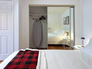 Ein Hotelzimmer mit einem Bett, einer rot-schwarz karierten Decke, einem hängenden Bügeleisen und einem Nachttisch mit Lampe.